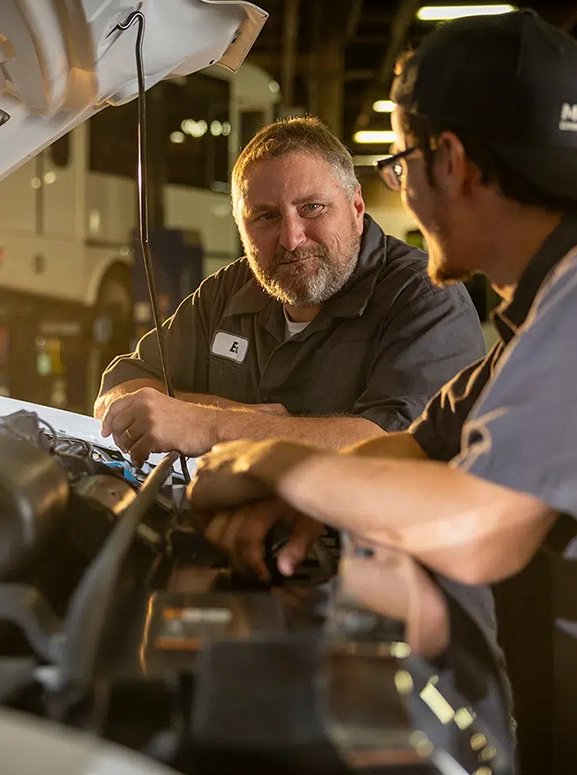 two mechanics chatting under a hood of a car